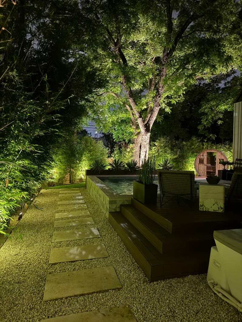 A Texas home at dusk with warm landscape lighting washing the stone, the oaks, and the front walk
